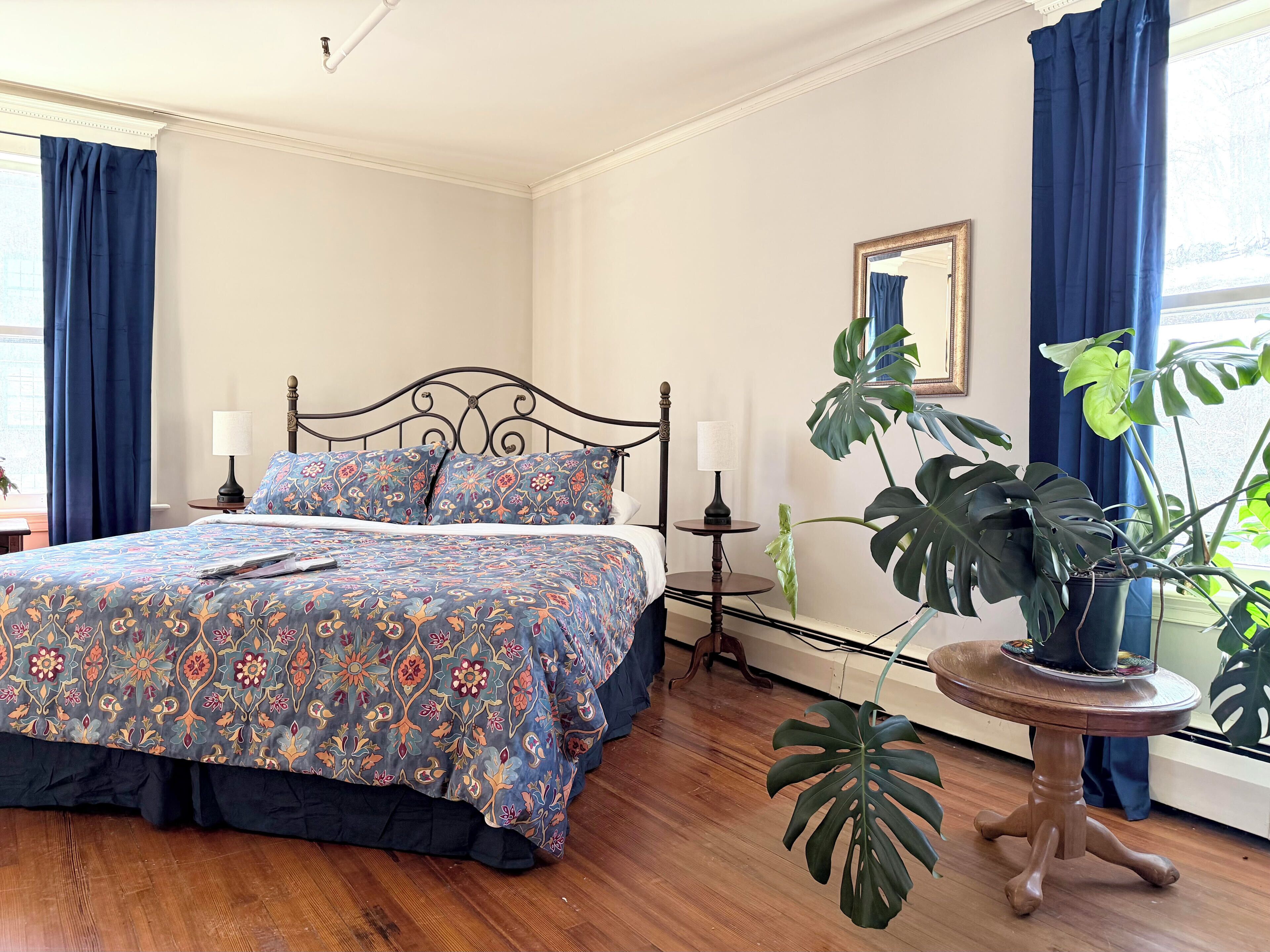 Un dormitorio con cama, dos mesitas de noche, una planta en maceta y una ventana con cortinas.