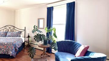 Une chambre à coucher avec un lit, un fauteuil bleu, une petite table et une plante en pot.