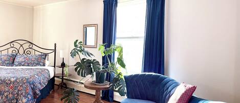 Une chambre à coucher avec un lit, un fauteuil bleu, une petite table et une plante en pot.