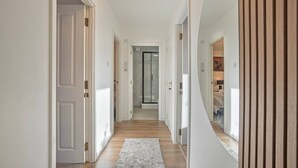 A hallway with white walls, wooden flooring, and a rug.