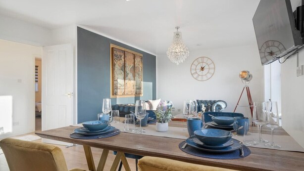 A modern dining area with a wooden table set for four, blue dinnerware, and a chandelier.