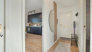A hallway leading to a kitchen with wooden flooring, a white door, and a mirror on the wall.
