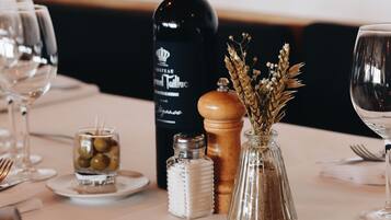 A dining table set with a bottle of Château Moutaut wine, a salt and pepper shaker, a small glass with olives, and a vase with dried flowers.