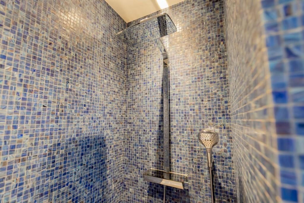 A bathroom with mosaic blue tiles on the walls and a shower area with a glass door.