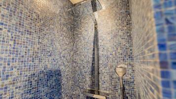 A bathroom with mosaic blue tiles on the walls and a shower area with a glass door.