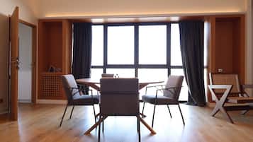 A modern dining area with a wooden table and four chairs, large windows with curtains, and a wooden floor.