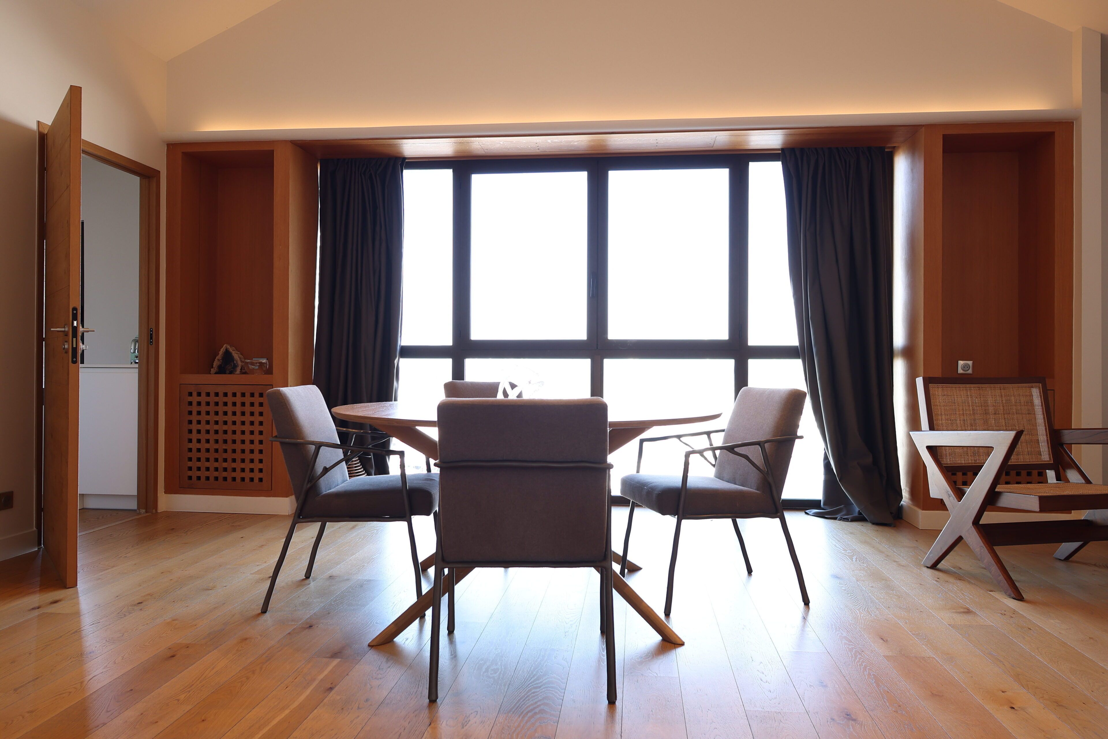 Uma sala de jantar moderna com uma mesa de madeira e quatro cadeiras, janelas amplas com cortinas e piso de madeira.