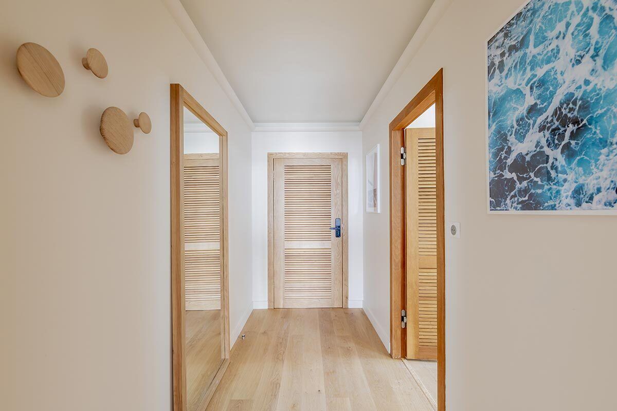 Un pasillo con puertas de madera, piso de madera y una obra de arte colgada en la pared.