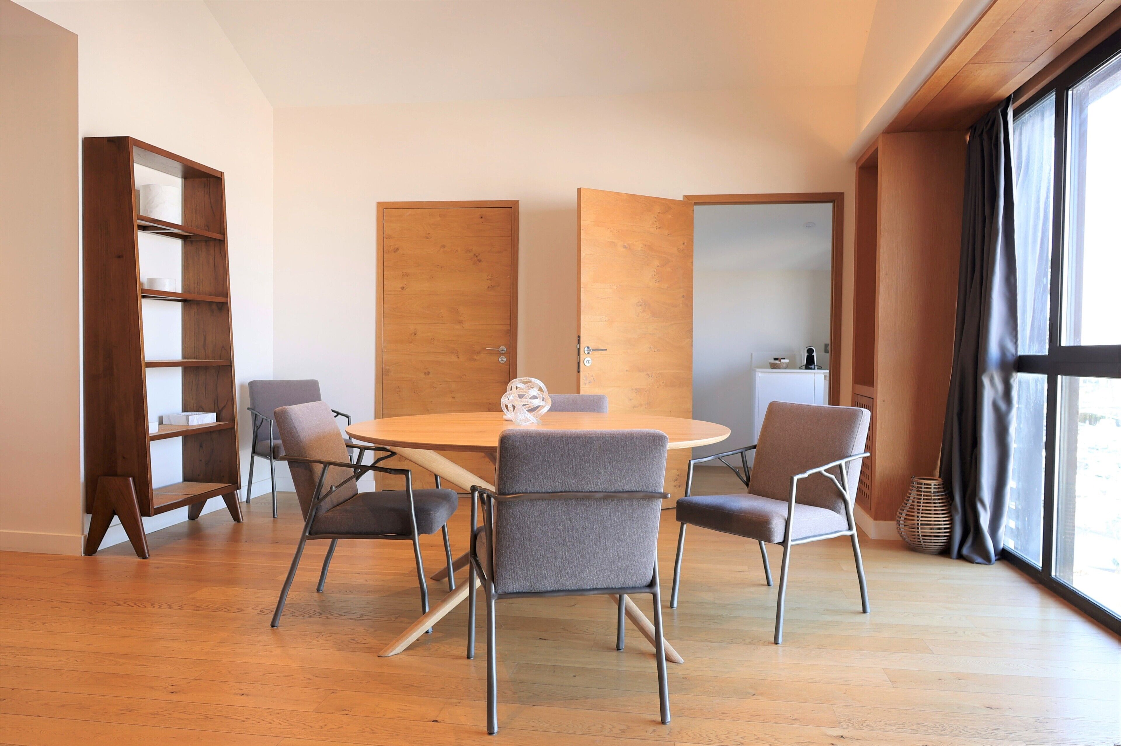 Un comedor moderno con una mesa redonda, cuatro sillas grises y una estantería de madera.