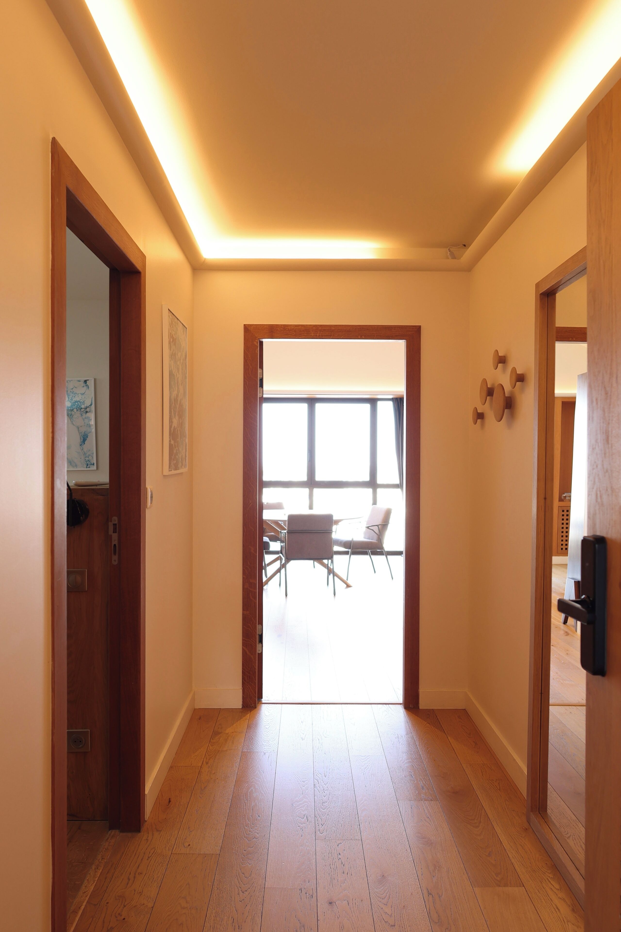 Un pasillo con suelo de madera, una puerta a la izquierda y vistas hacia un comedor con sillas y una mesa.