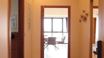 Un pasillo con suelo de madera, una puerta a la izquierda y vistas hacia un comedor con sillas y una mesa.