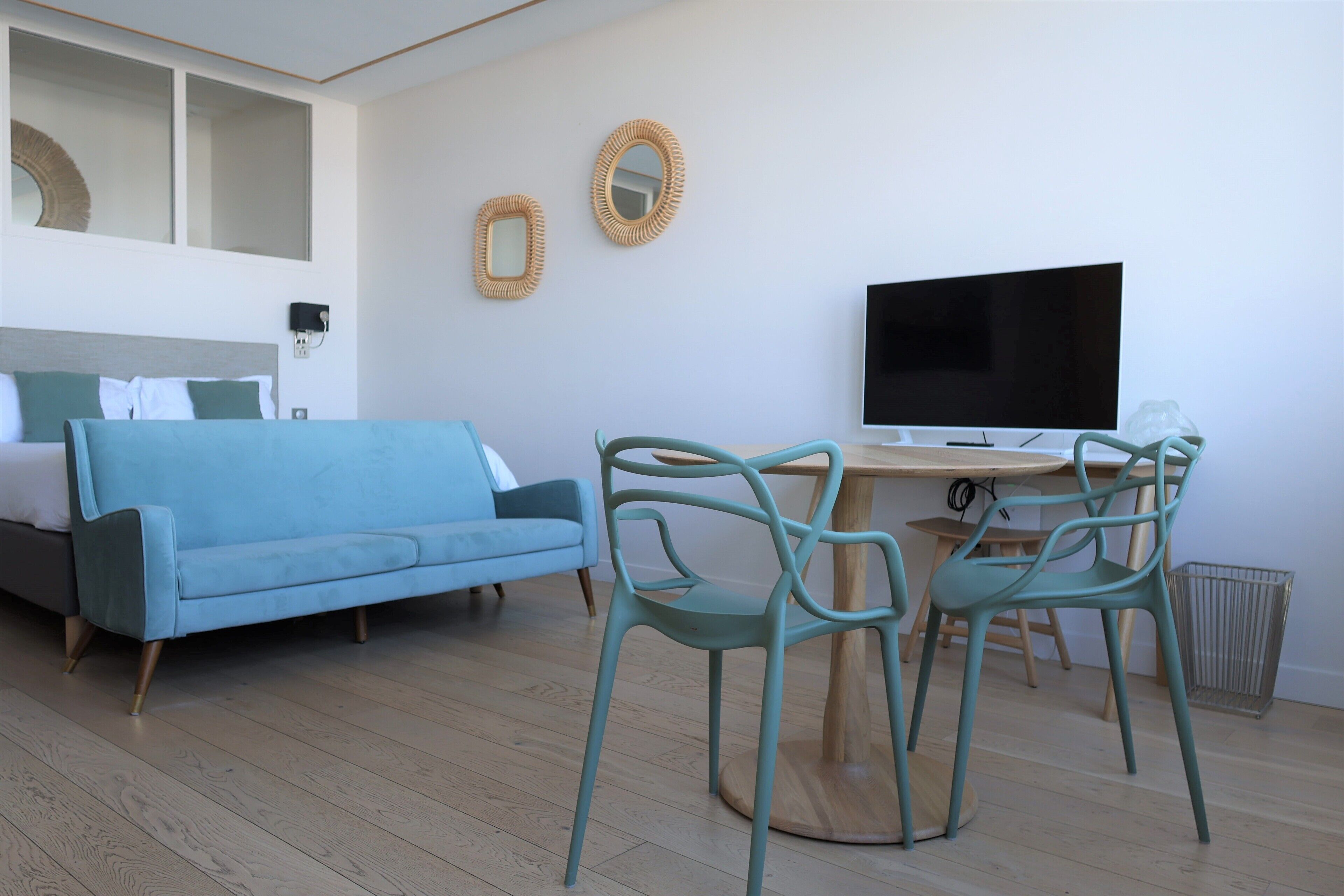 Een moderne kamer met een blauwe bank, blauwgroene fauteuils, een houten eettafel en een televisie aan de muur.