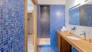 Un baño moderno con mosaicos azules, un mueble de tocador de madera, un espejo grande y una zona de ducha.
