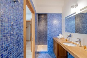 Un baño moderno con mosaicos azules, un mueble de tocador de madera, un espejo grande y una zona de ducha.