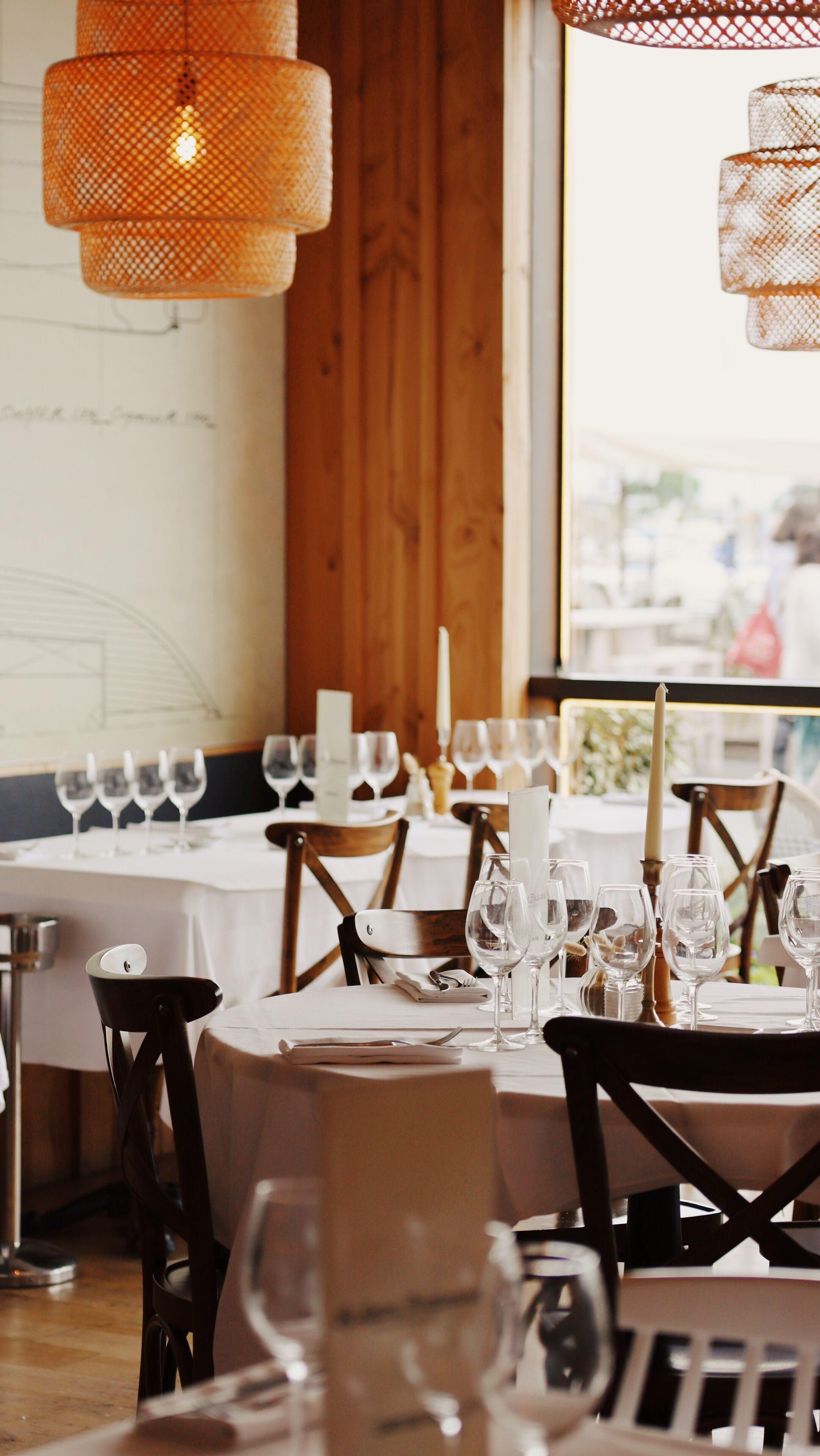 Ein Restaurantinneres mit Holzwänden, einem großen Fenster und gedeckten Tischen mit Weingläsern und Kerzen.