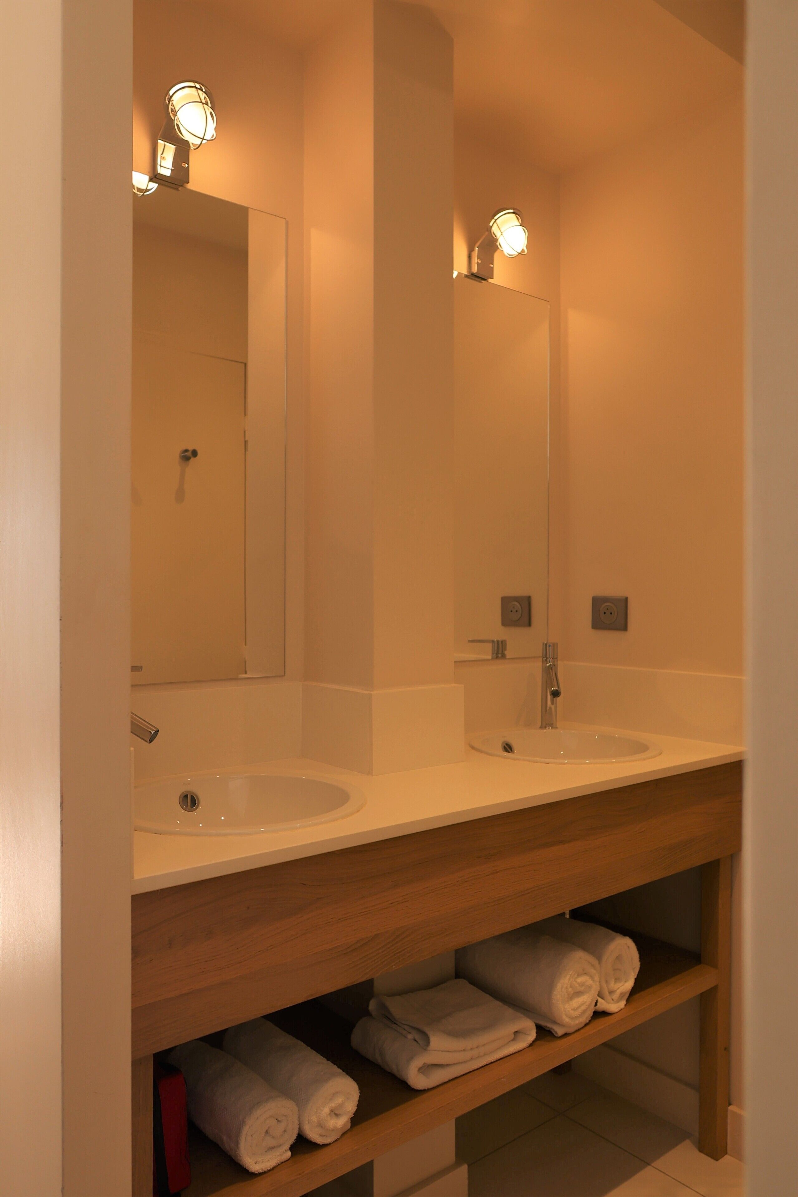 Een badkamer met twee wastafels, een spiegel en planken met handdoeken.