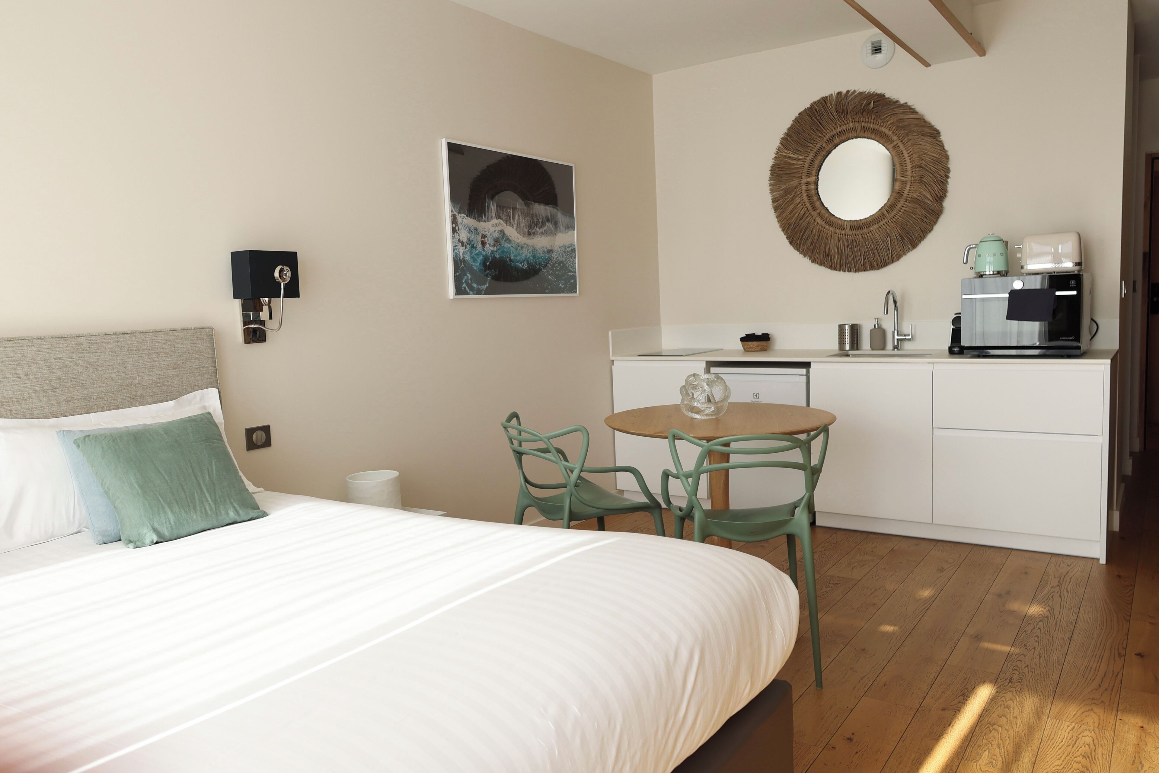 Un dormitorio con cama, una mesa redonda con sillas, una cafetera y un espejo montado en la pared.