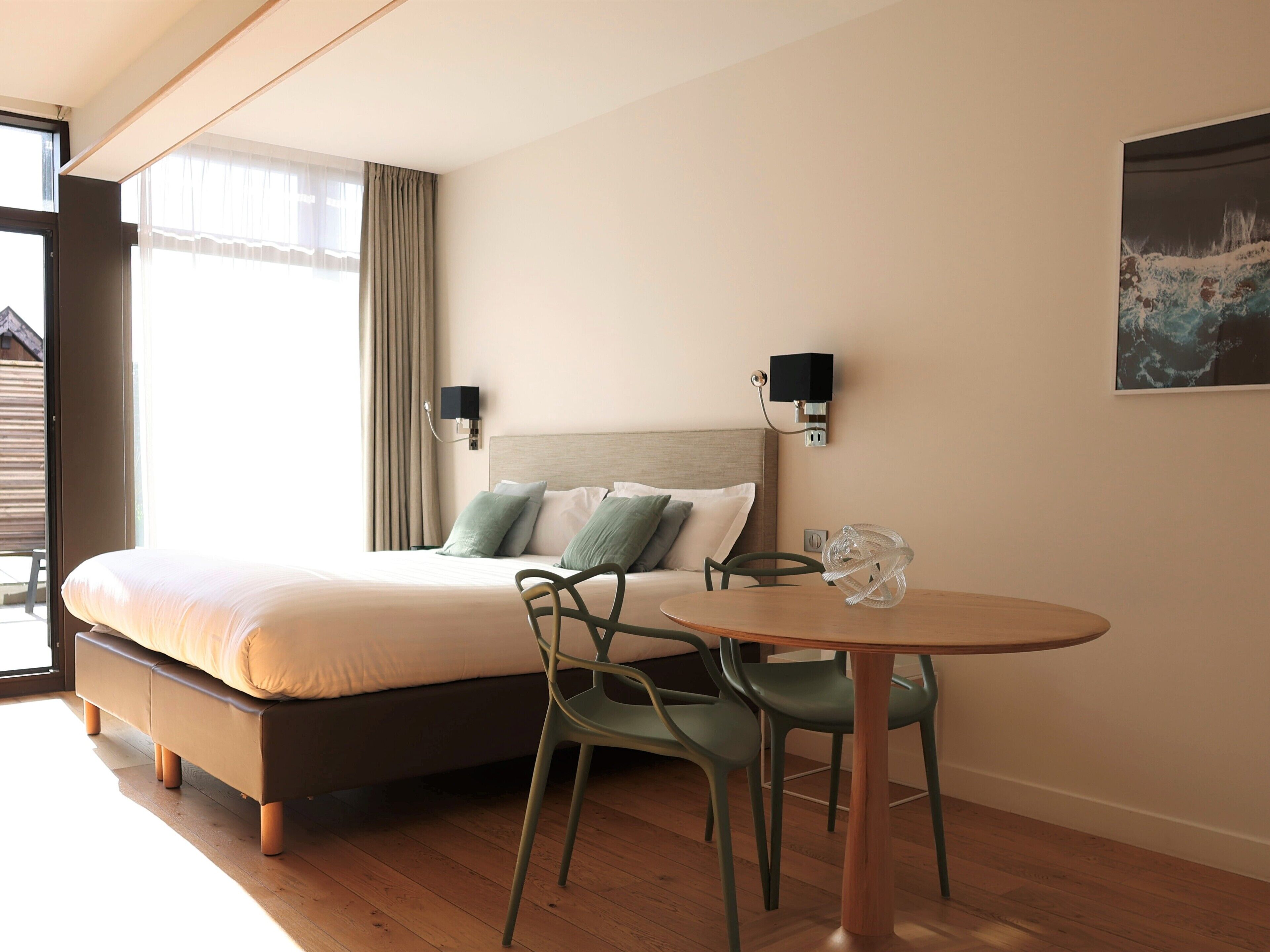 Een hotelkamer met een bed, twee wandlampen, een tafel met stoelen en een schilderij aan de muur.