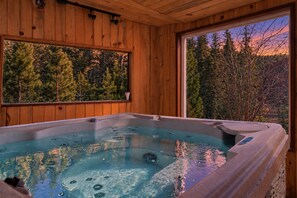 A hot tub with a wooden interior and a view of trees through a window.