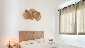 A bedroom with a tufted headboard, a bedside table with a lamp, and a window with curtains.