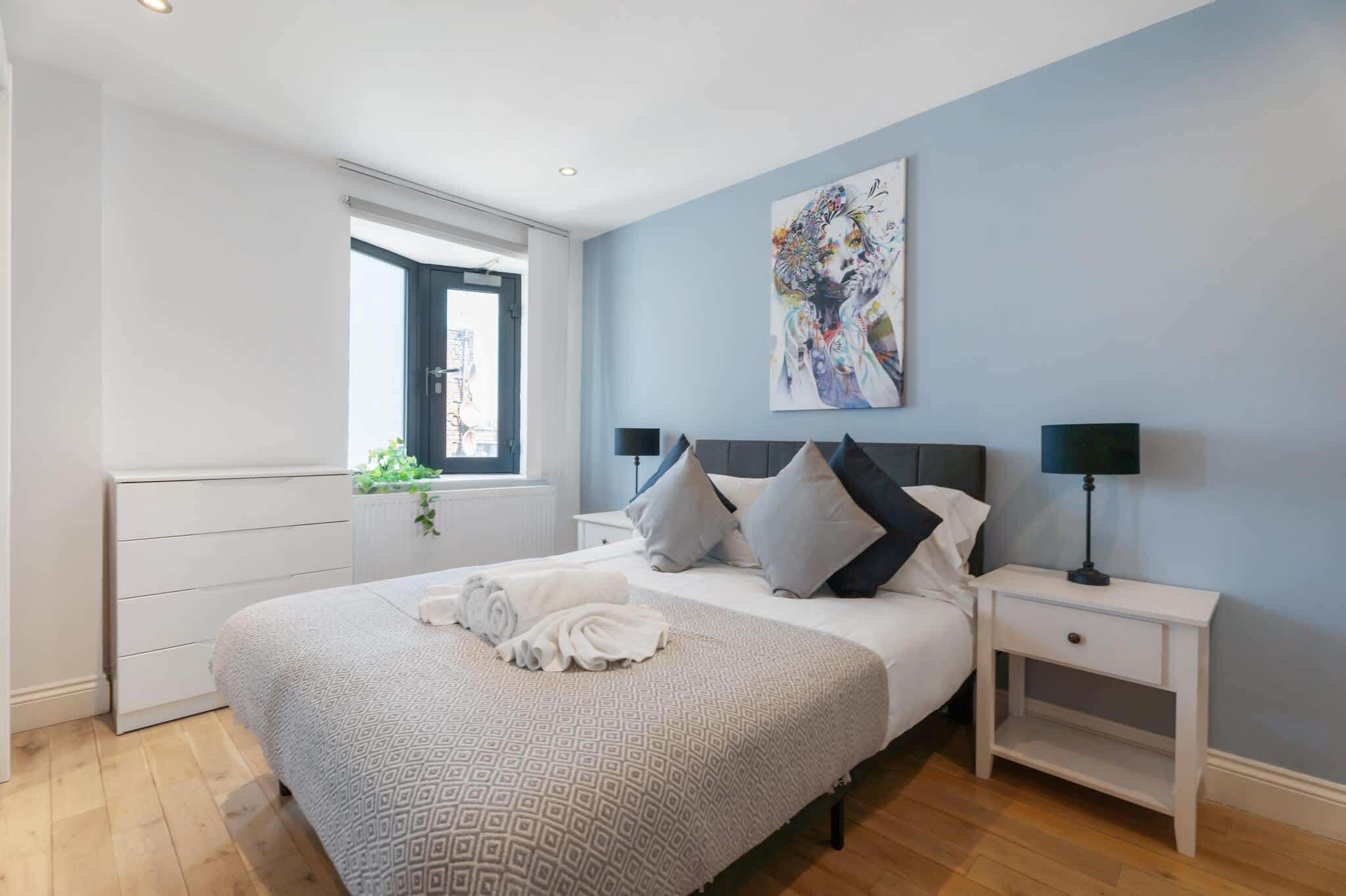 A bedroom with a bed, bedside tables, a window, and a painting on the wall.