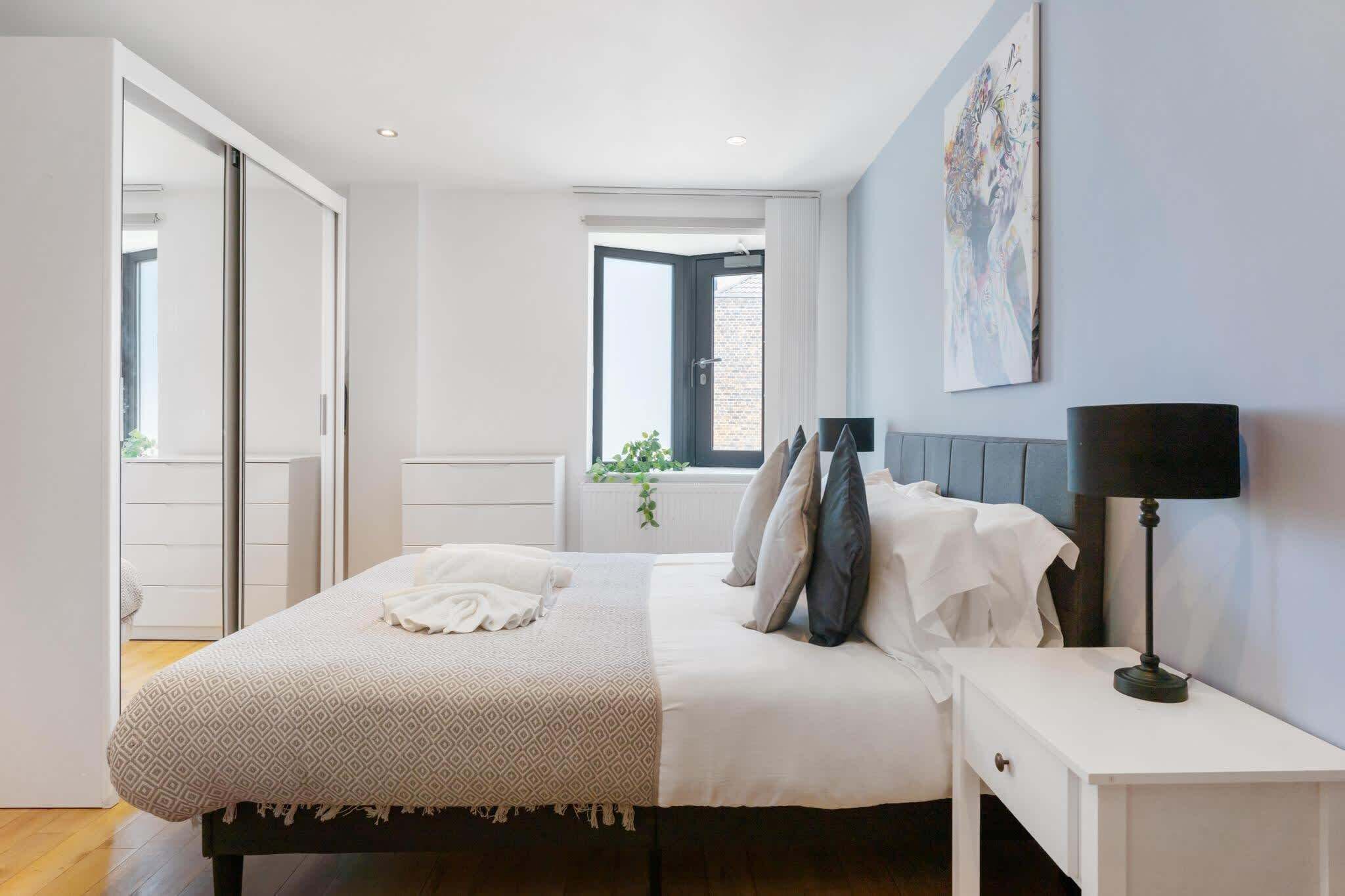 Een slaapkamer met een bed, nachtkastjes, een raam en een schilderij aan de muur.