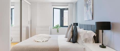 A bedroom with a bed, bedside tables, a window, and a painting on the wall.