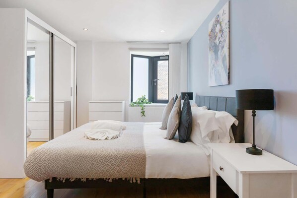 Un dormitorio con cama, mesitas de noche, una ventana y un cuadro en la pared.