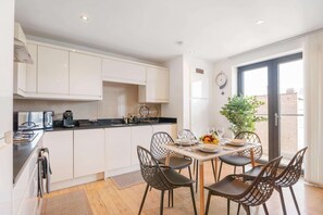 Een moderne keuken met witte kasten, een eettafel gedekt voor vier personen, en een groot raam met uitzicht op gebouwen.