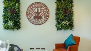 Una habitación con una mesa redonda, una única silla naranja con un cojín azul y dos decoraciones verticales verdes en la pared.