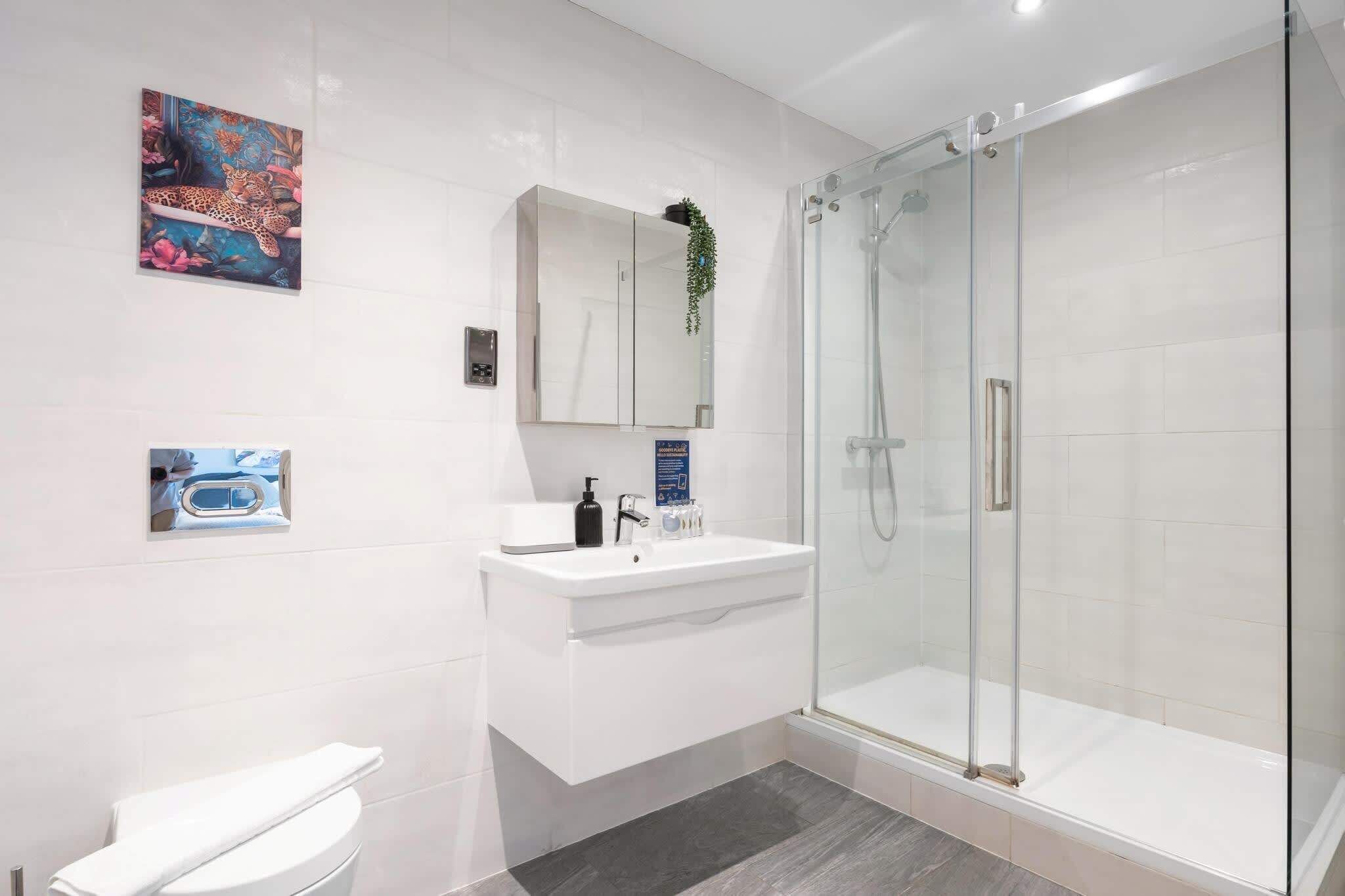Un baño moderno con ducha envuelta en vidrio, un lavamanos blanco y un inodoro.