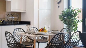 Comedor con una mesa dispuesta para cuatro, sillas, un frutero y un reloj de pared.