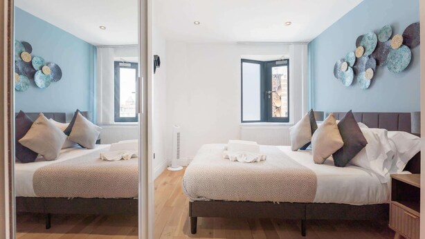 Habitación con espejos, dos camas, un ventanal y una lámpara fijada a la pared.