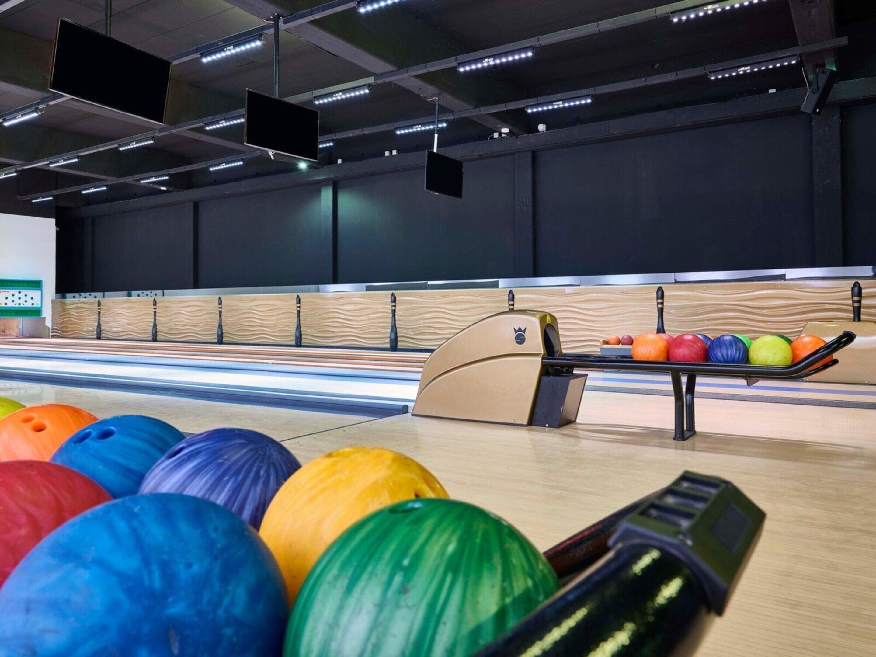 A bowling alley with multiple lanes, a bowling ball rack, and overhead lighting.