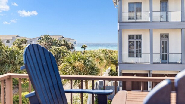 A beachfront property with a balcony, a view of the ocean, and palm trees.