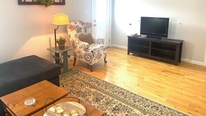 A living room with a sofa, a coffee table, a TV stand, a lamp, and a patterned rug. - Long term chic en suite 2 bedroom Corp Rental in N. Knox/Powell with WiFi, AC (Powell)