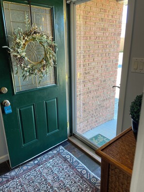 A green door with a wreath, a patterned rug, and a brick wall visible through the door. - Long term chic en suite 2 bedroom Corp Rental in N. Knox/Powell with WiFi, AC (Powell)