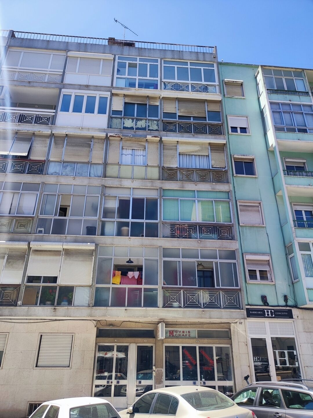 A multi-story building with balconies, a ground-level shop, and parked cars.