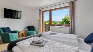 Een slaapkamer met twee bedden, een aan de muur bevestigde televisie en uitzicht op groen.