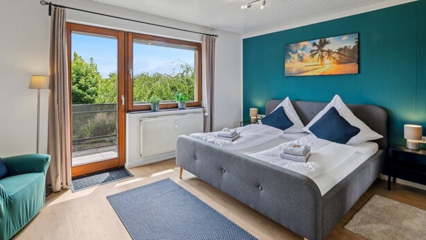 Een slaapkamer met een groot bed, uitzicht op groen door een raam en een schilderij aan de muur.