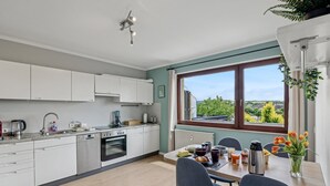 Een moderne keuken met witte kasten, een inbouwoven en een eethoek met een tafel gedekt voor twee personen.