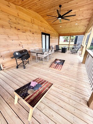 A covered outdoor patio with a wooden deck, a barbecue grill, wicker furniture, and a ceiling fan. - Elegant Retreat • King Bed • Expansive Deck • Peaceful Escape •  Fireplace (Crossville)