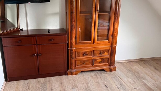 A bedroom with a wooden wardrobe, a television on a stand, and a bed with a blue and white duvet. - NR 4 DG 2 rooms for companies and families (Nieder Vellmar)