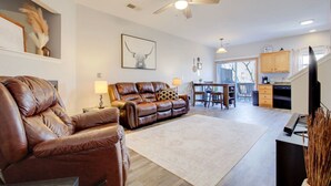 A spacious living area with a brown leather sofa, a dining table with chairs, a ceiling fan, and a kitchen area with wooden cabinets. - 2 Kings, Workspace, Garage 3bdrm - Pastore`s Place (Manhattan)