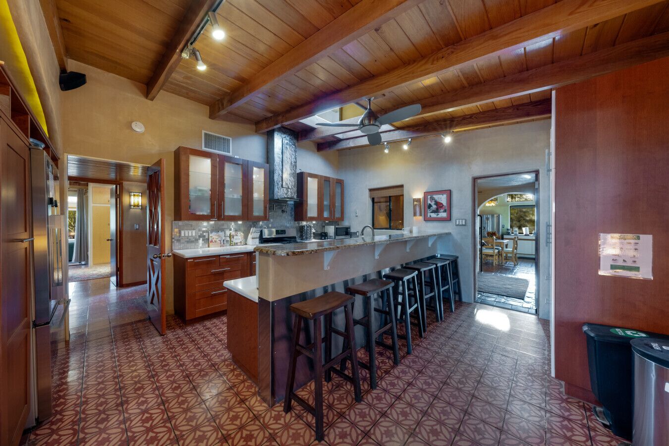 Una cucina con isola centrale, sgabelli da bar, mobili in legno e pavimento piastrellato decorato.