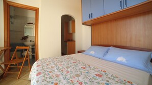Ein Schlafzimmer mit Bett, Holzschrank und einem durch eine offene Tür erreichbaren Badezimmer.