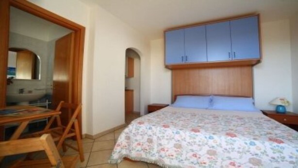A bedroom with a bed, wooden headboard, a desk with a chair, a mirror, and a wardrobe.