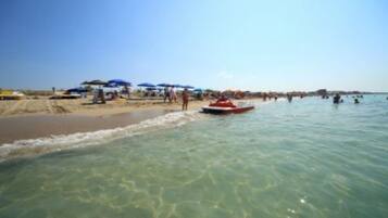 Une plage avec une eau cristalline, des parasols et un jet ski.