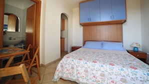 Ein Schlafzimmer mit Bett, Holz-Kopfteil, Nachttisch, Tisch mit Stühlen, Spiegel und Kleiderschrank.