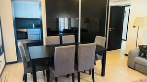 A modern dining area with a black table and six chairs, a kitchen in the background, and a sofa with a lamp. - NocasHouse Porto (Campo)